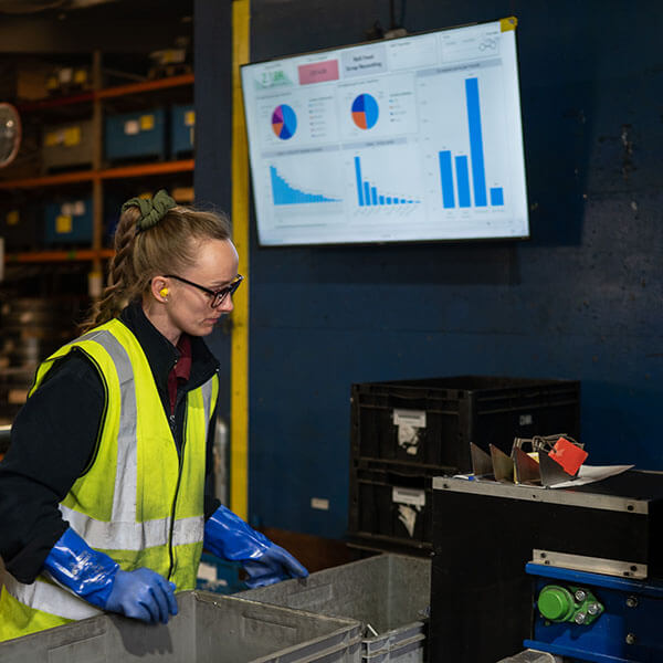 A factory worker in safety gear sorts materials. A screen showing information on a factory digitalisation. 